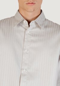 Camicia di seta grigio chiaro con righe verticali, colletto button-down e bottoni bianchi. Tessuto morbido e design aderente.