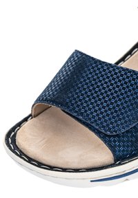 Open-toe sandal with blue textured fabric strap and beige cushioned footbed on white sole with stitching detail.