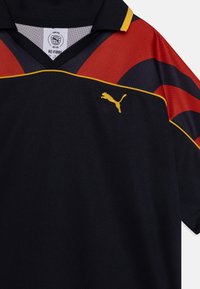 Svart polo-skjorte med røde og marineblå striper, gullkant og gull Puma-logo på venstre bryst. Laget av pustende stoff.