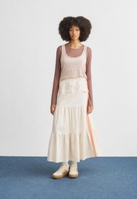 Cream-colored, tiered maxi skirt with orange side stripes, paired with a light brown long-sleeve top and white sneakers. Textured fabric.