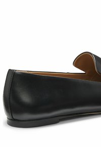 Zwart leren platte schoen met een afgeronde neus, instapmodel en een beige voering, gezien vanuit een zijaanzicht tegen een witte achtergrond.