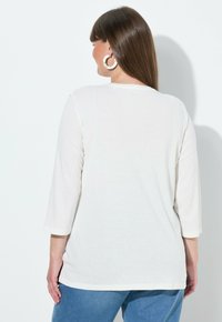 Bílá bavlněná košile s dlouhým rukávem, kulatým výstřihem a rukávy do půli paže, spojená s modrými džínami z denimu. Jednoduchý a neformální design.