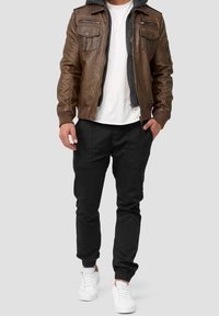 Chaqueta bomber de cuero marrón con bolsillos con cremallera sobre una camiseta blanca, combinada con pantalones negros ajustados y zapatillas blancas.