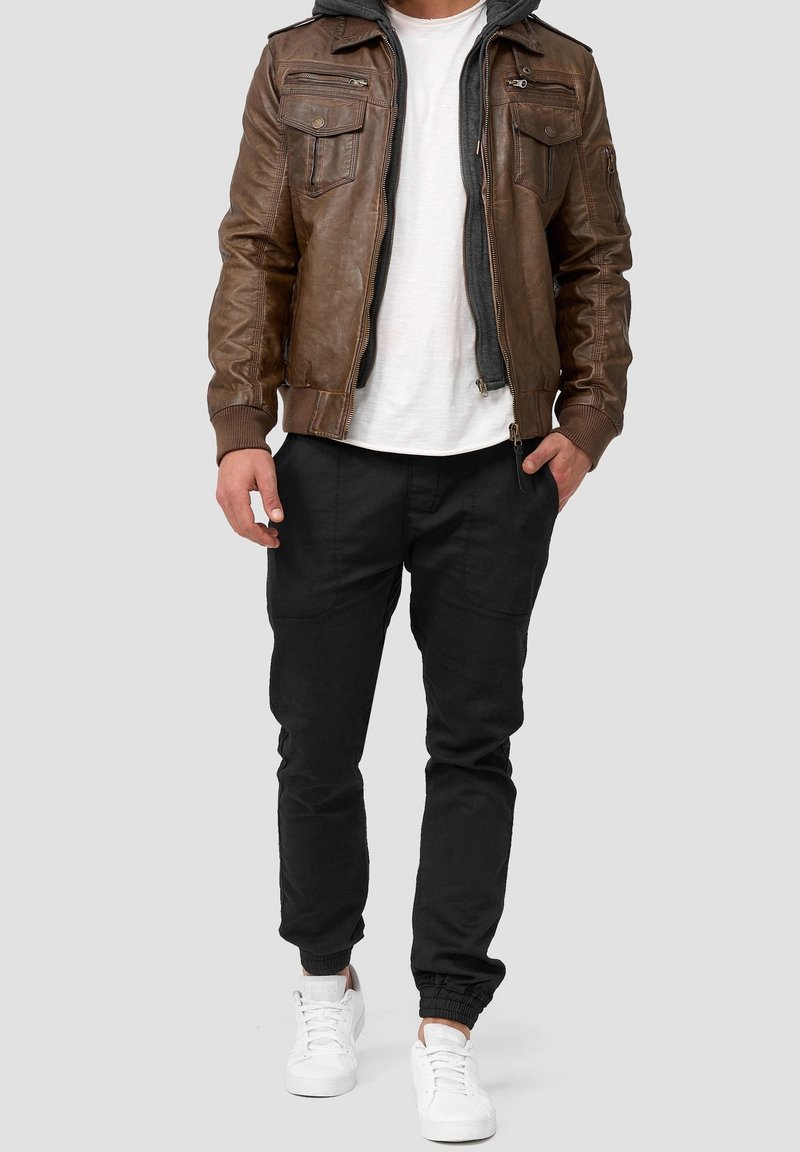 Chaqueta bomber de cuero marrón con bolsillos con cremallera sobre una camiseta blanca, combinada con pantalones negros ajustados y zapatillas blancas.