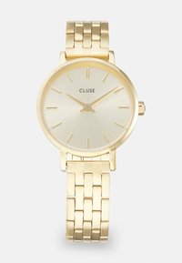 Gold metal wristwatch with a pale gold sunburst dial, featuring thin hour markers and a polished mesh bracelet. Brand name "CLUSE" displayed.