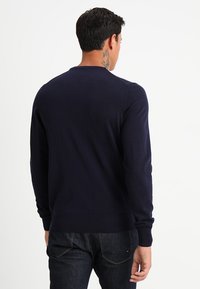 Granatowy sweter z dzianiny z okrągłym dekoltem, prążkowanymi mankietami i dołem, o textured powierzchni, noszony na ciemnych dżinsach. Gładki widok z tyłu.