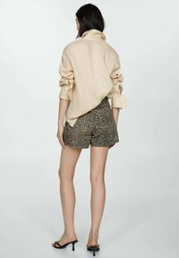 Camicia di lino beige con maniche arrotolate, abbinata a pantaloni corti a stampa leopardata scura. Il modello indossa tacchi neri con cinghie. Sfondo neutro.