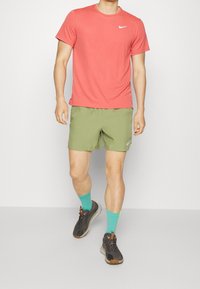 Red Nike t-shirt, crew neck, paired with olive green shorts. Teal socks and black shoes with orange accents complete the athletic outfit.