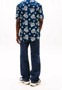 Short-sleeve navy shirt with white floral print; paired with loose-fitting navy pants and patterned sneakers.