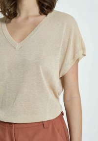Beige pletený top s véčkovým výstřihem a krátkými rukávy, měkká textura, kombinovaný s kalhotami v barvě rezavé s detalem knoflíku.
