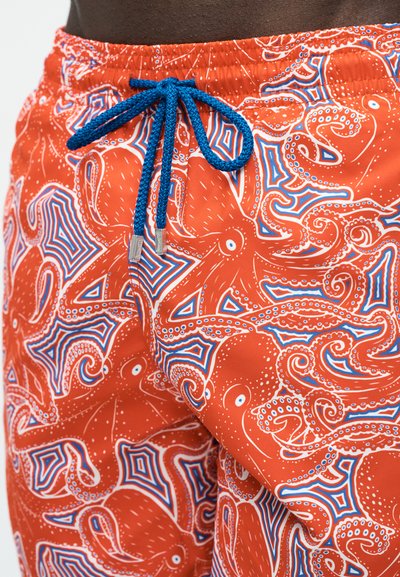 Κοντινό πλάνο πορτοκαλί μαγιό σορτς με μπλε εκτύπωση χταποδιού και σκουρόχρωμο μπλε πλεκτό κορδόνι δεμένο μπροστά.