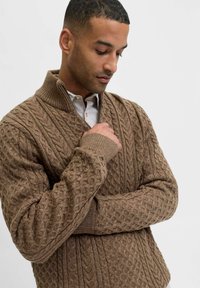 Brauner Strickpullover mit strukturierten Mustern und hohem Kragen. Verfügt über gerippte Bündchen und einen Reißverschluss, was dem Design zusätzliche Tiefe verleiht.