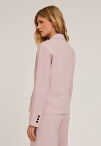 Blazer rosa chiaro con colletto a scollo, tasca singola e tre bottoni neri su ciascun polsino. Tessuto liscio con vestibilità su misura.