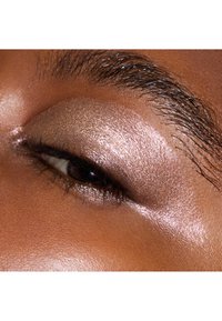 Shimmery eyeshadow in a warm bronze tone applied to the eyelid, with a smooth texture and reflecting light, highlighting the brow area.