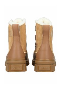 Brązowe botki z zamszu i skóry ze białym futerkiem z imitacji, wysokim cholewkiem i teksturowaną gumową podeszwą. Na pięcie znajduje się logo marki.
