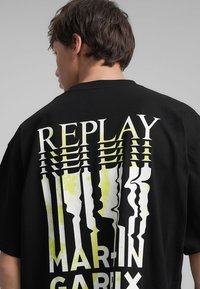 T-shirt oversize nera con testo bianco e verde lime audace e distorto sul retro: "REPLAY MARTIN GARRIX." Tessuto morbido.