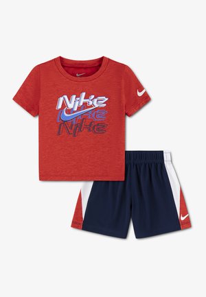 Rood Nike T-shirt met korte mouwen, voorzien van gelaagde logotekst en swoosh, gecombineerd met marineblauwe, witte en rode Nike shorts.