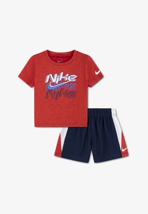 Red short-sleeve Nike T-shirt with layered logo text and swoosh, paired with navy blue, white, and red Nike shorts.