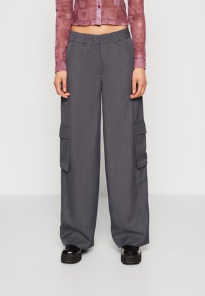 Person iført grå vidbenede cargobukser med klaplommer og sorte platformsko, kombineret med en cropped lyserød gennemsigtig top.