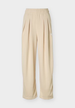 Pantalon beige taille haute à jambes larges avec ceinture élastique et plis sur le devant, arborant un logo discret sur le côté.