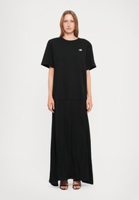 Black maxi dress with short sleeves, made of soft fabric, features a round neckline and a logo detail on the chest. Smooth texture.