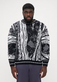 Black and white knit sweater featuring intricate patterns, textured fabric, crew neck, and ribbed cuffs. The design includes abstract elements.