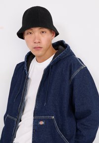 Denimjakke med blå tone, grå indvendig, justerbare snore og frontlommer. Sort ribbet bøttehat komplimenterer looket.