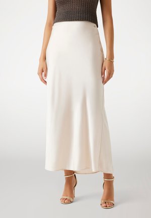 Jupe maxi en satin crème avec une texture lisse, taille haute, dotée d'une fente sur le côté, associée à des sandales à talons hauts dorées avec des lanières.