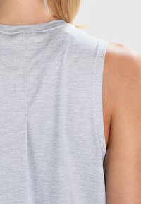 Top sin mangas de color gris claro hecho de tela suave, con escote redondo y un ajuste holgado, con costuras visibles y detalles de textura.