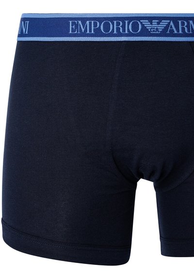 Men's boxer briefs in navy fabric, featuring a blue elastic waistband with "Emporio Armani" logo. Smooth texture, fitted design, and mid-length cut.