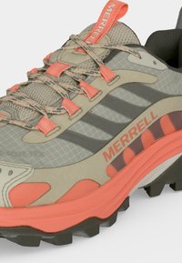 Gros plan sur une chaussure de randonnée Merrell beige et corail avec un mesh texturé, des lacets à motifs et une semelle noire robuste conçue pour une utilisation en extérieur.