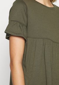 Olivově zelený bavlněný top s krátkými volány, stahovaným pasem a kulatým výstřihem s dekorativním prošíváním.