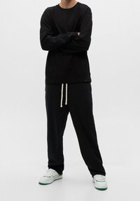 Svart sweatshirt med långa ärmar och rundad halsringning, parat med löst sittande svarta byxor med dragsnöre. Vita sneakers fulländar looken.