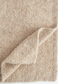 Tessuto beige morbido con una superficie testurizzata e un bordo leggermente arricciato, che presenta un aspetto caldo e accogliente.