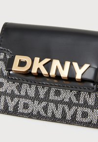 Portafoglio nero lucido con logo "DKNY" dorato, caratterizzato da un design in tessuto nero e bianco testurizzato. Forma compatta con materiali a contrasto.