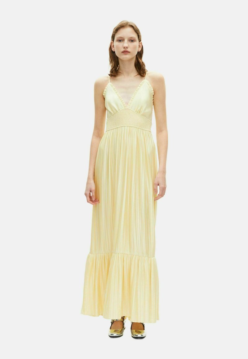 Maxi dress gialla a righe con spalline sottili, scollatura arricciata, corpetto elasticizzato smock e orlo svasato. Modella che indossa scarpe dorate.