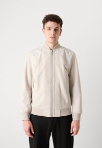 Heled beige bomber-jakk, millel on tõmblukk, küljetaskud, soonikkoes varrukad ja alläär. Sile nahkatunne, minimalistlik disain.