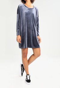 Grå sammet långärmad klänning med rundad halsringning, sidofickor och en avslappnad passform, tillsammans med svartvita sneakers.