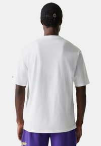 T-shirt in cotone bianco con una vestibilità rilassata. Maniche corte, scollatura rotonda e retro semplice. Indossato con pantaloni corti viola con testo sull'orlo.