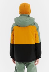 Kleurblokjack met gele, groene en zwarte panelen, met een capuchon en elastische manchet. Gemaakt met een bijpassende groene muts.