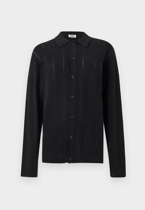 Camisa negra de manga larga con botones, con sutiles patrones verticales de tejido y un cuello clásico, presentada sobre un fondo blanco liso.