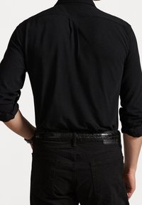 Zwart shirt met lange mouwen en een boord met knoopsluiting, gemaakt van een gestructureerde stof, met opgerolde manchetten, gecombineerd met een zwarte broek en een glanzende zwarte riem.