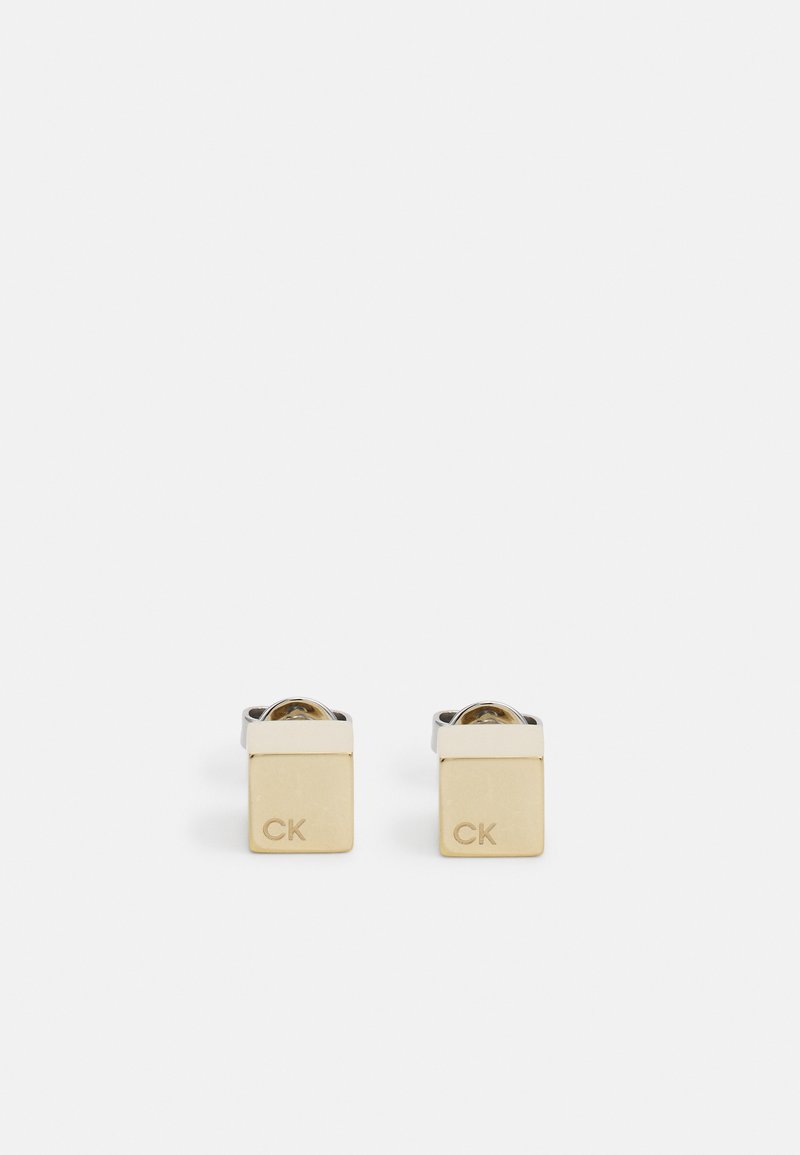 Gemelli in oro e argento con design quadrato, incisi "CK", con finitura lucida e un dettaglio centrale circolare trasparente.
