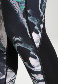 Primer plano de leggings negros con patrones de calaveras abstractos y distorsionados en colores, y costuras visibles sobre un fondo claro.