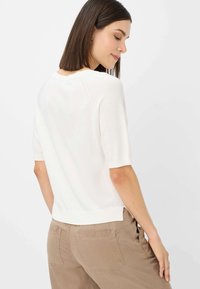 Kortærmet hvid sweater i et let, strikket materiale, med en rund halsudskæring og en lidt cropped kant. Behagelig pasform.