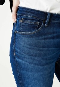 Los jeans de mezclilla azul cuentan con un diseño clásico de cinco bolsillos, con un ajuste ceñido, un sutil desgastado y detalles cosidos a lo largo de las costuras.