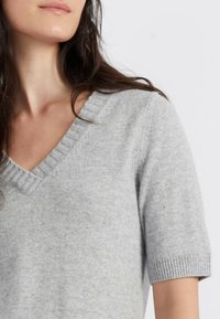 Maglione grigio chiaro a maniche corte con scollatura a V e dettaglio a costine sul collo e sui orli delle maniche, realizzato in un morbido materiale testurizzato.