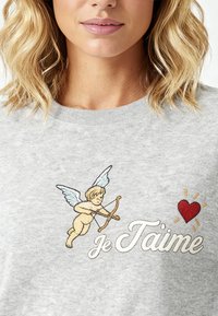 Grijze trui met een geborduurde putto met vleugels, boog en hart, vergezeld van de tekst "je t’aime" in sierlijke letters.