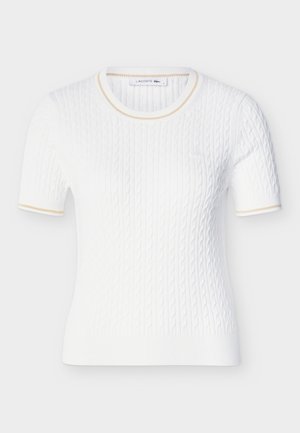 Haut blanc en maille à manches courtes avec motif torsadé, encolure ronde, bordure beige subtile sur le col et les bords des manches, et petit logo brodé sur la poitrine.