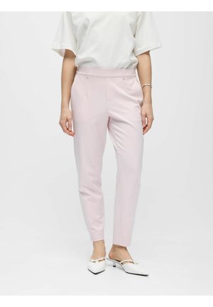 Kvinde iført lyserøde skræddersyede bukser, hvid kortærmet top, hvide lavhælede spidse sko og et sølvarmbånd.